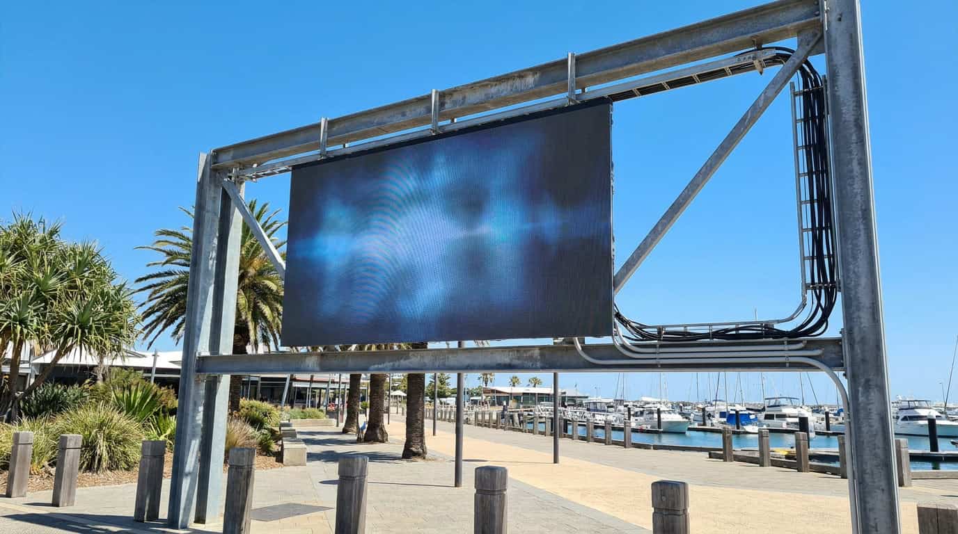 Outdoor LED display mounted on a steel frame beside a waterfront