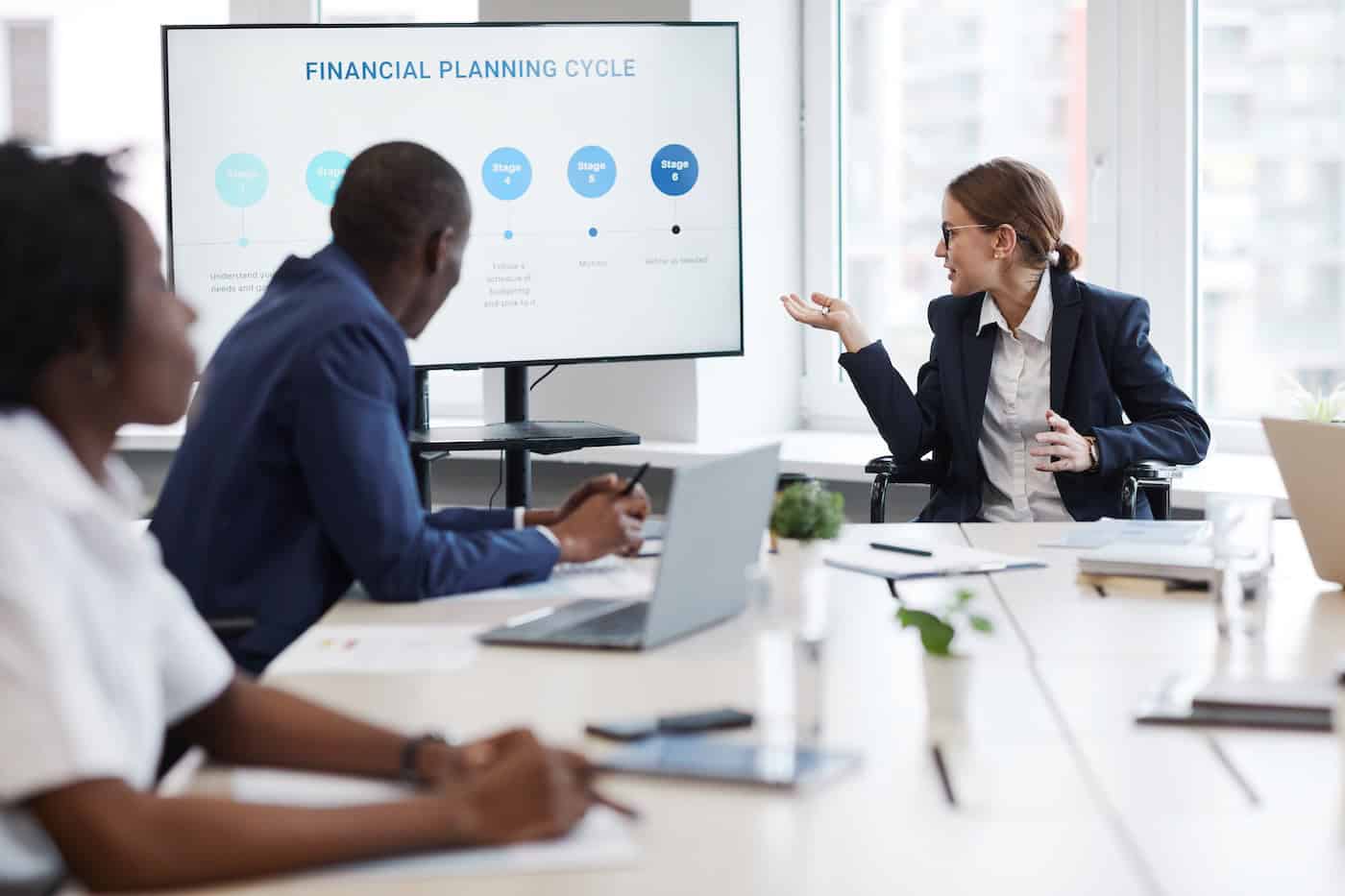 Workplace discussion around a table with a financial presentation on screen