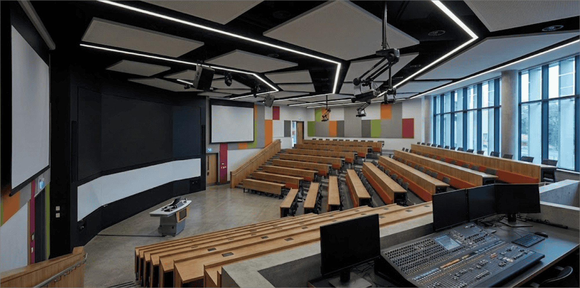 Large tiered lecture theatre with projection screens, a lectern and an AV control desk
